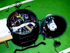 Abbildung 3: Ein Blick unter die Haube von Gonzales: Im Deckel (rechts) sind die Halterung und der Stellmotor für die Firewire-Kamera zu sehen, links der Robot-Körper von vorn. Trotz CAN-Bus und eines IBM-Notebooks als Steuerrechner ist die Verkabelung überaus komplex.