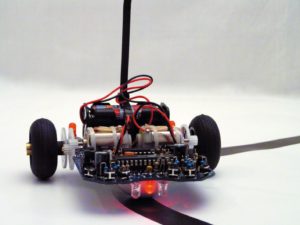 Abbildung 4: Die rote LED auf der Unterseite der Platine liegt direkt auf, während die beiden transparenten Fototransistoren etwas abstehen. Über die Reflexion auf dem Untergrund kann der Roboter eine dunkle Linie verfolgen.
