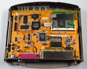 E Abbildung 4: Der Asus- Router von innen. Das WLAN-Modul ist herausnehmbar im Mini-PCI-Slot rechts oben untergebracht, links in der Mitte sitzt der 20-polige Busanschluss für Erweiterungen. Die hochintegrierte MIPS-CPU ist genau dazwischen eingelötet.