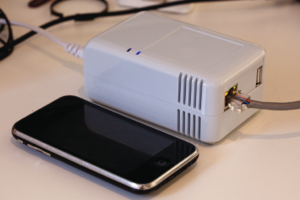 Abbildung 2: Ein Sheevaplug-Minirechner, wie er in der vorgestellten Heizungssteuerung zum Einsatz kommt, im Größenvergleich zu einem I-Phone.